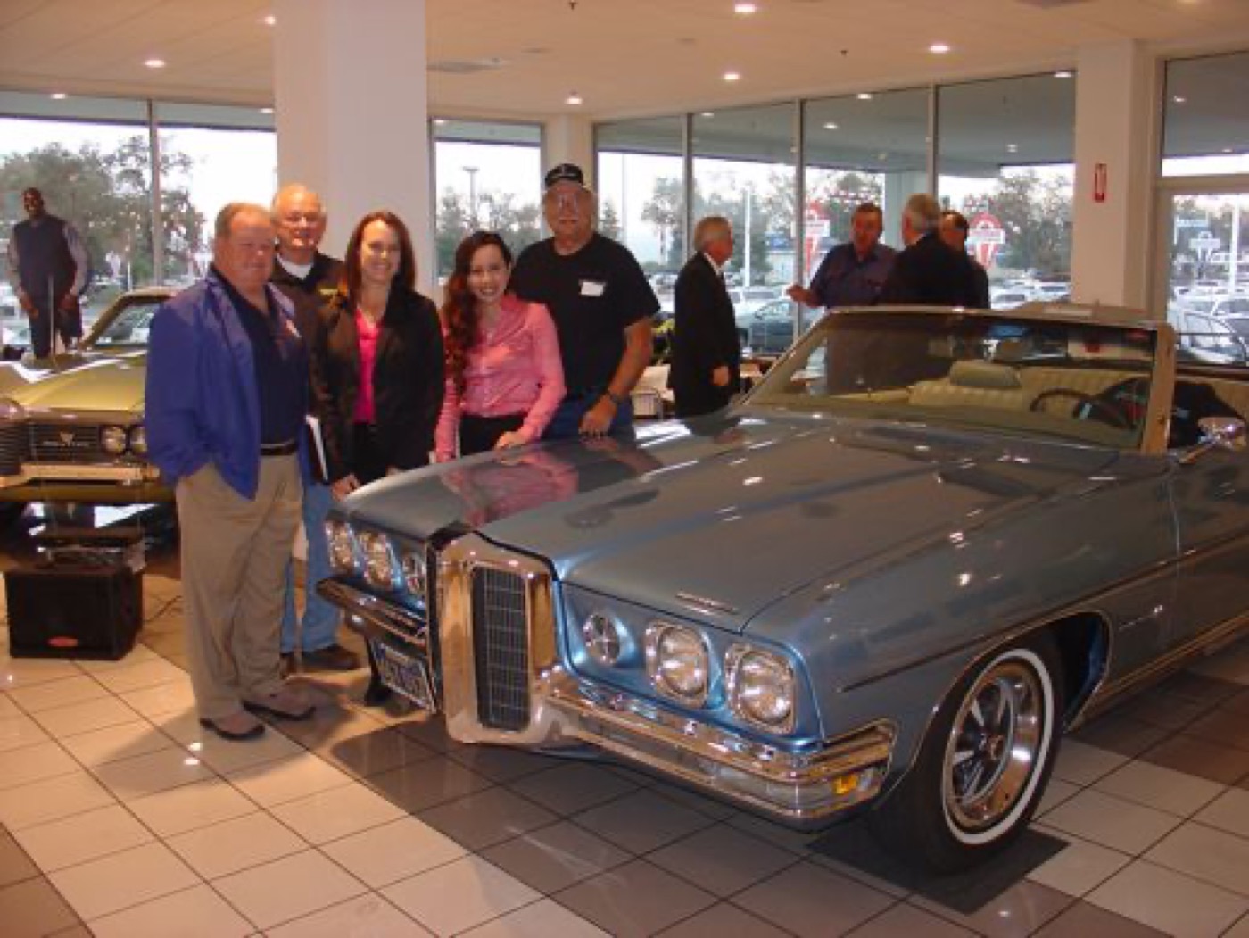 Smiling members gathered around blue Pontiac convertible