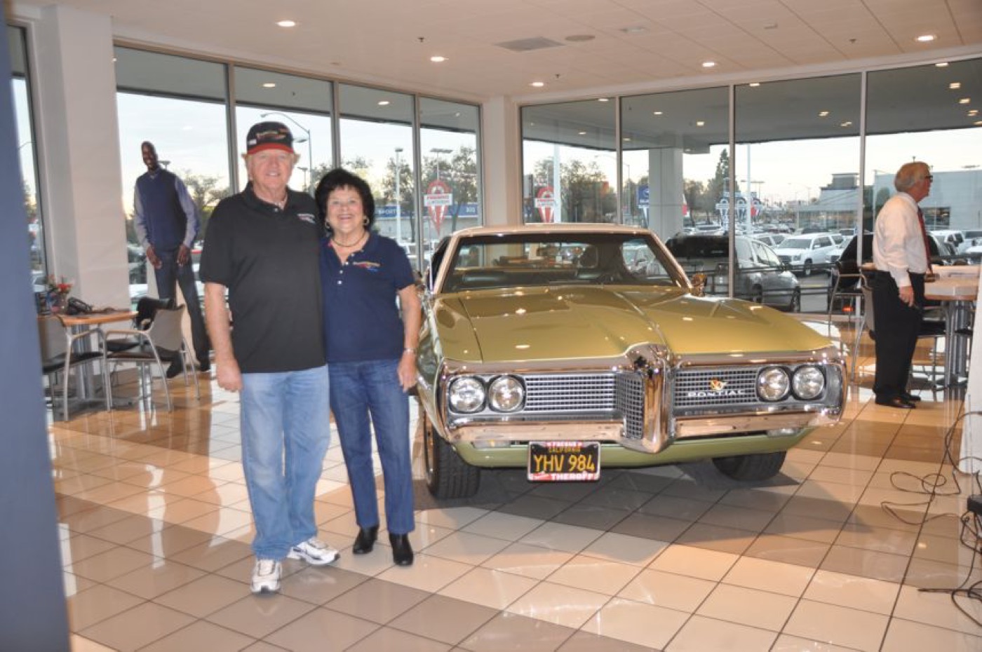 Happy couple beside golden Pontiac hardtop