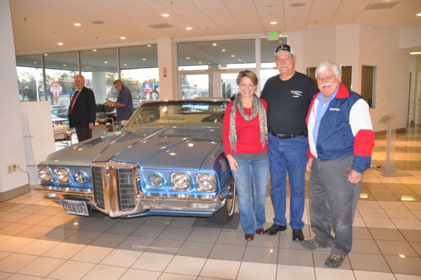 Smiling trio posing with classic blue Pontiac